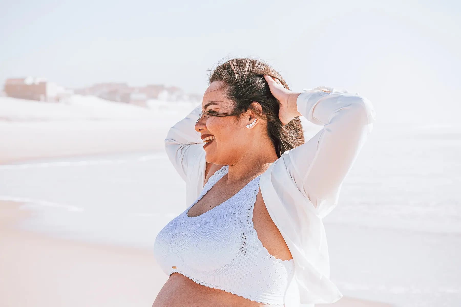 Grávida na praia a sorrir, numa sessão de maternidade