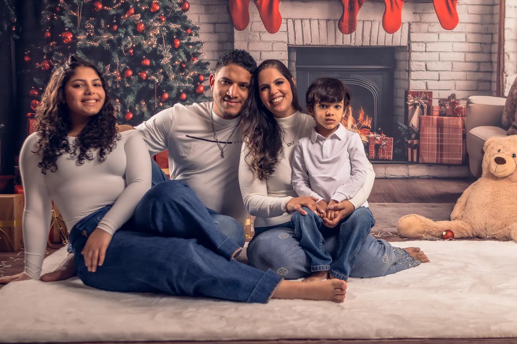 Família em tons de branco junto à lareira, numa sessão de Natal em estúdio